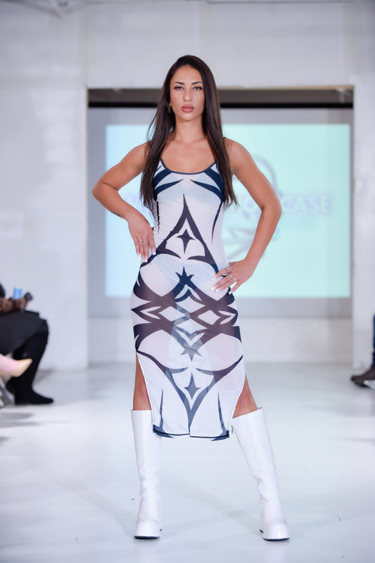 Model wearing a white and blue patterned dress with white knee-high boots on a runway.