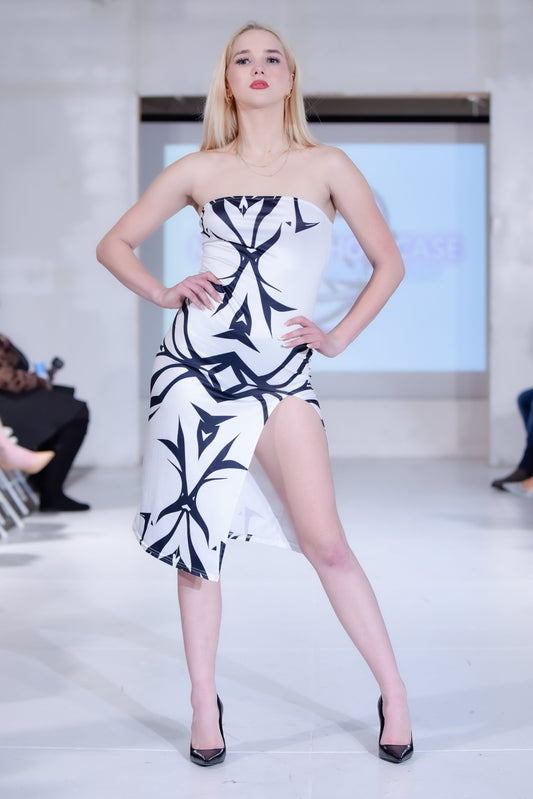 Model wearing a black and white strapless dress on a runway with an audience in the background.